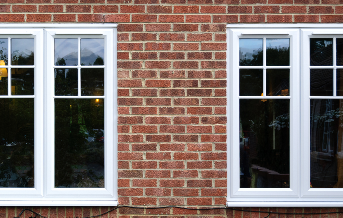 Two white uPVC windows in a red brick house.