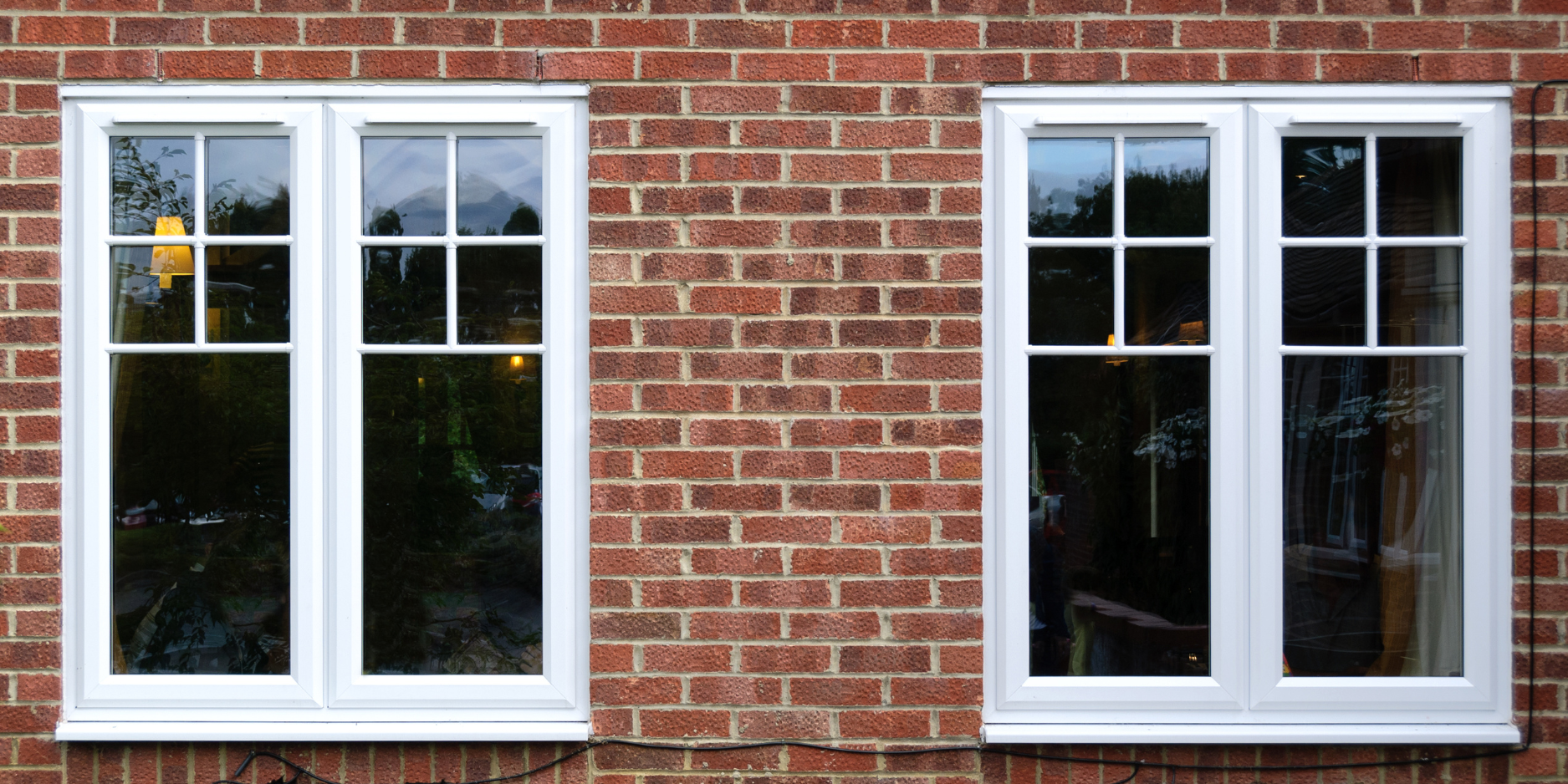 Two white uPVC windows in a red brick house.